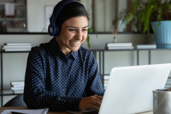 Head shot happy young indian ethnicity female manager wearing wireless headphones, looking at laptop screen, holding pleasant conversation with partners clients online, working remotely at workplace.