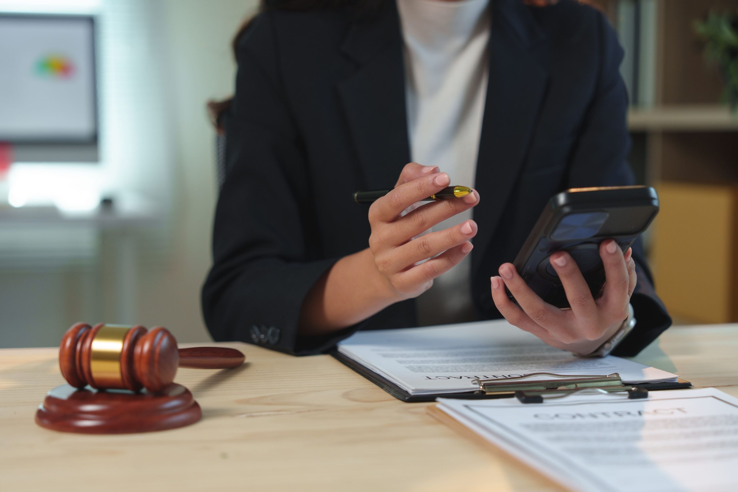 Female attorney reviewing legal documents while holding a phone and pen at her office desk