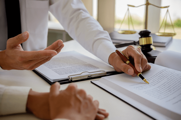 Young male lawyer in a modern law office standing at a desk with legal documents, a gavel, law books, and Lady Justice statue.