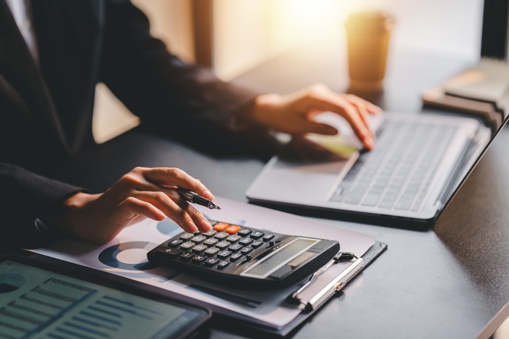 Person using calculator and laptop to analyze financial data