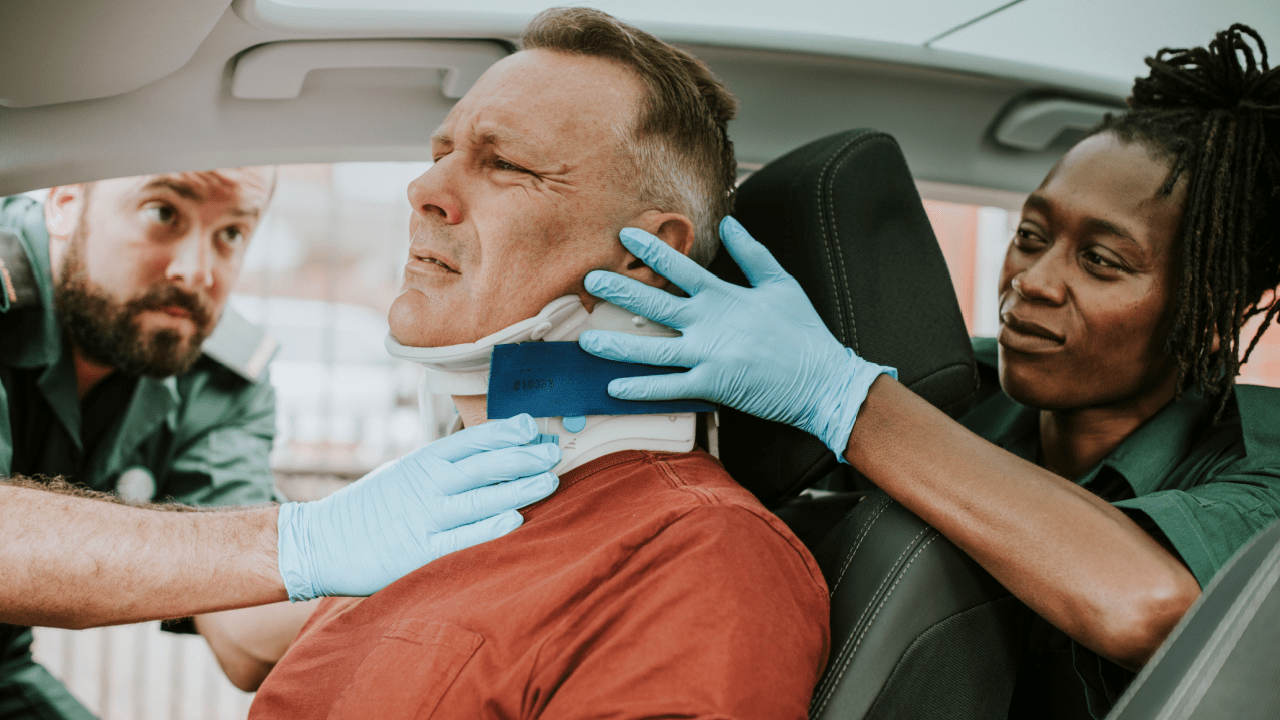 Paramedics placing a neck brace on an injured man after a crash — how do you get whiplash in a car accident