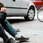Injured man sitting near a car and bike after accident – what is MVA whiplash