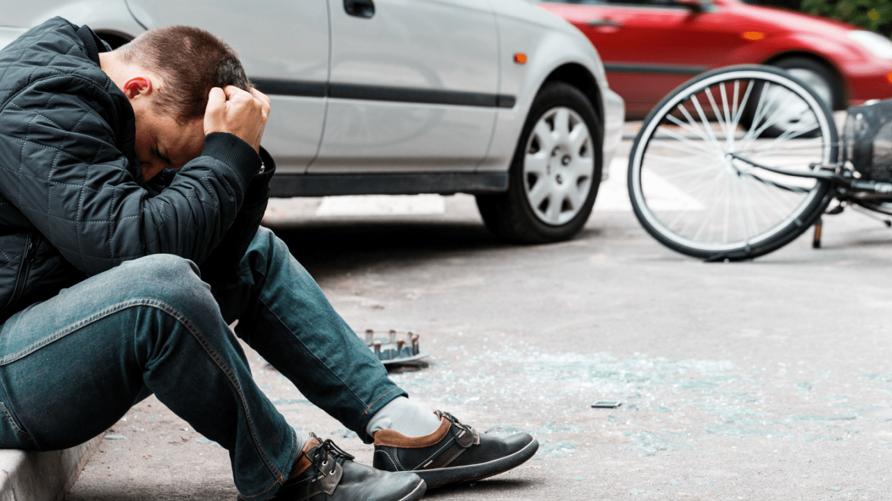 Injured man sitting near a car and bike after accident – what is MVA whiplash