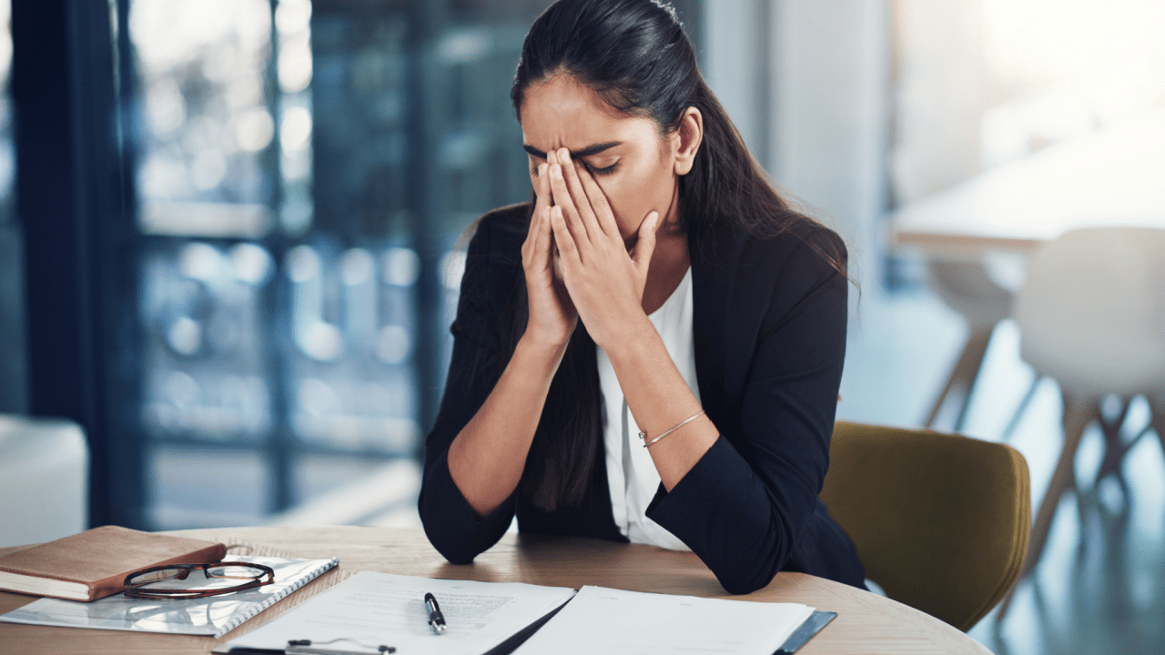 Stressed businesswoman covering face with hands while reviewing financial documents at desk, demonstrating the emotional challenge of learning how do you value items for bankruptcy