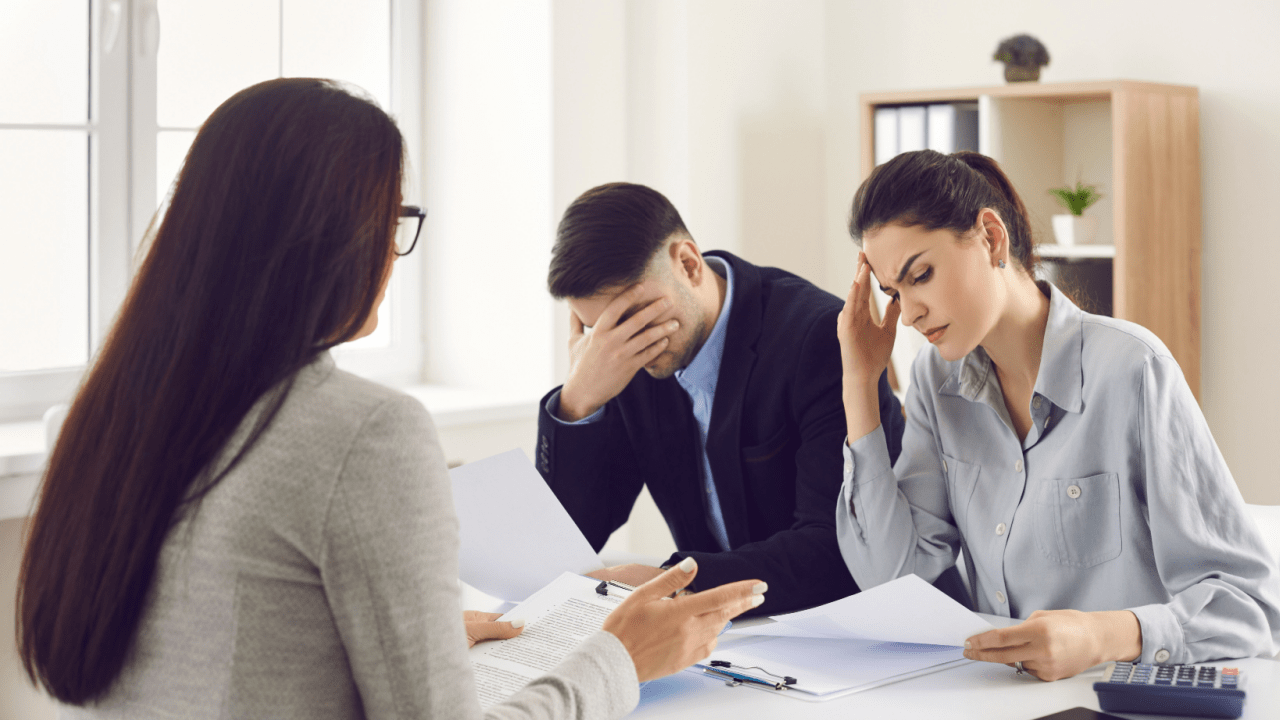 Stressed couple meeting with financial advisor reviewing documents, discussing how much is too much to make to file bankruptcy