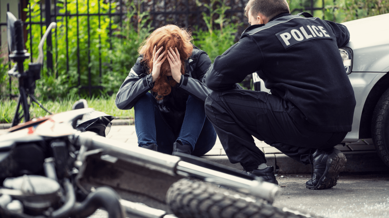 Police officer speaking with distressed woman after motorcycle crash – what is an MVA charge