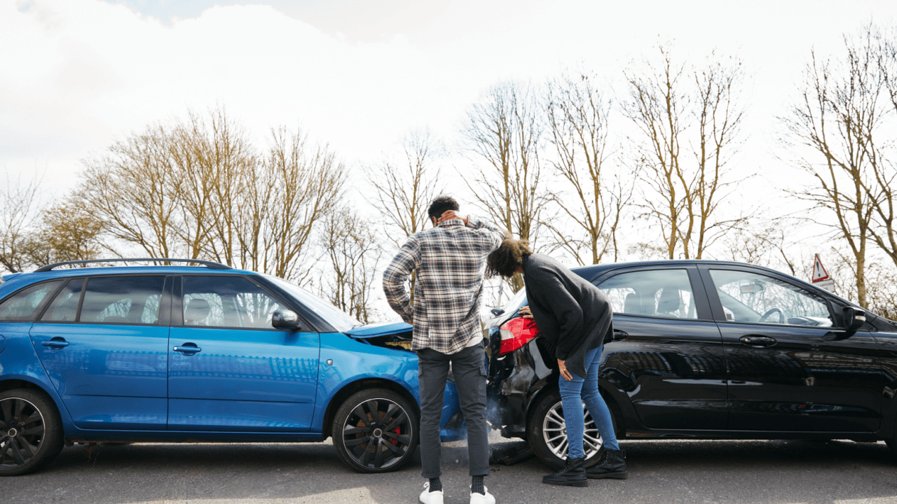 Two person examining rear-end collision damage between blue and black cars, showing what happens if someone wrecks your car and they aren't on your insurance Progressive