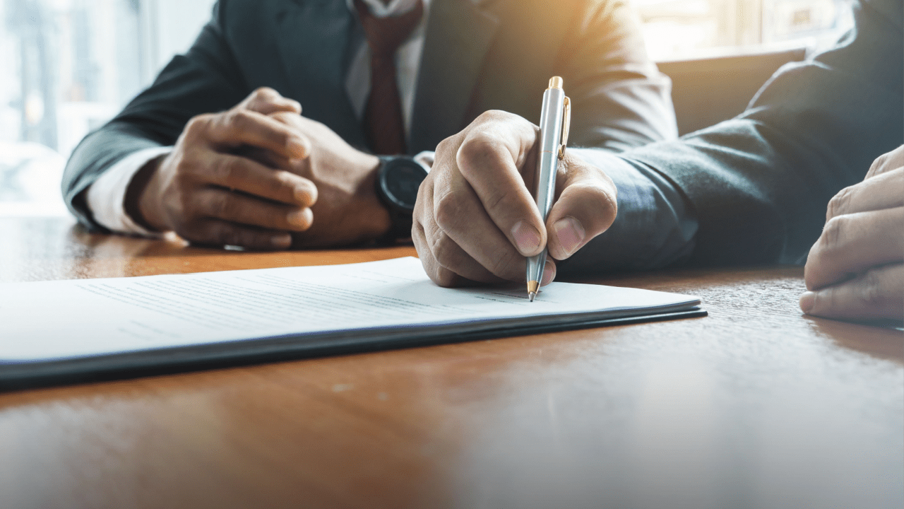 Business professional signing bankruptcy documents while another person observes, illustrating what happens when a customer files for bankruptcy