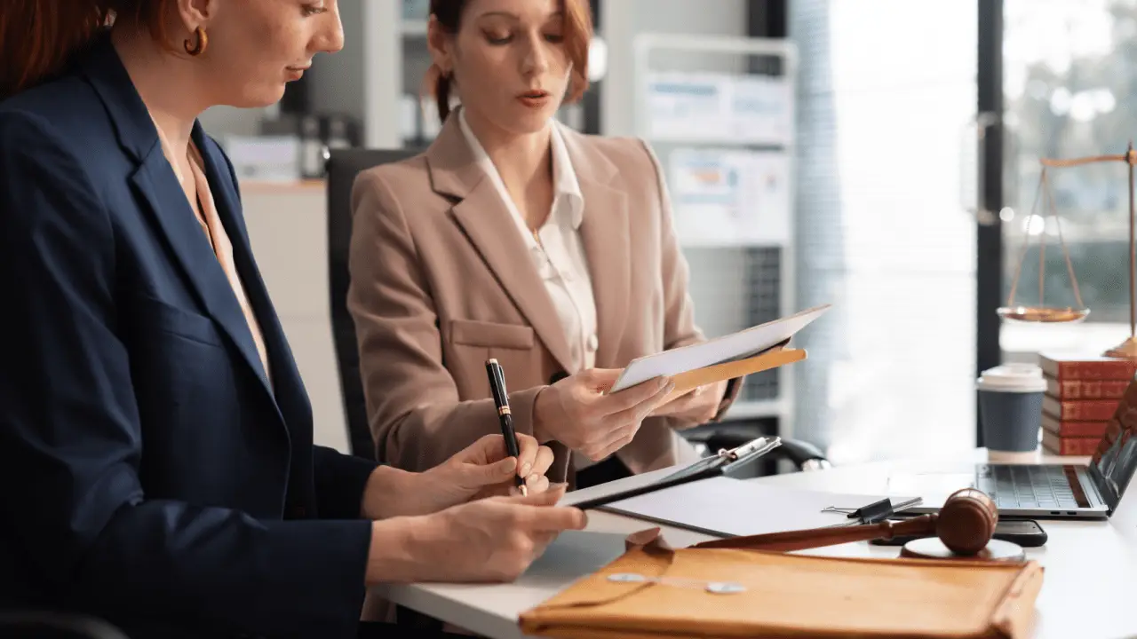 Two female attorneys collaborating on auto accident lead generation strategy while reviewing case documents in modern law office