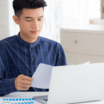 Young man reviewing financial documents on a laptop while considering if he should file bankruptcy for $20,000 in debt.