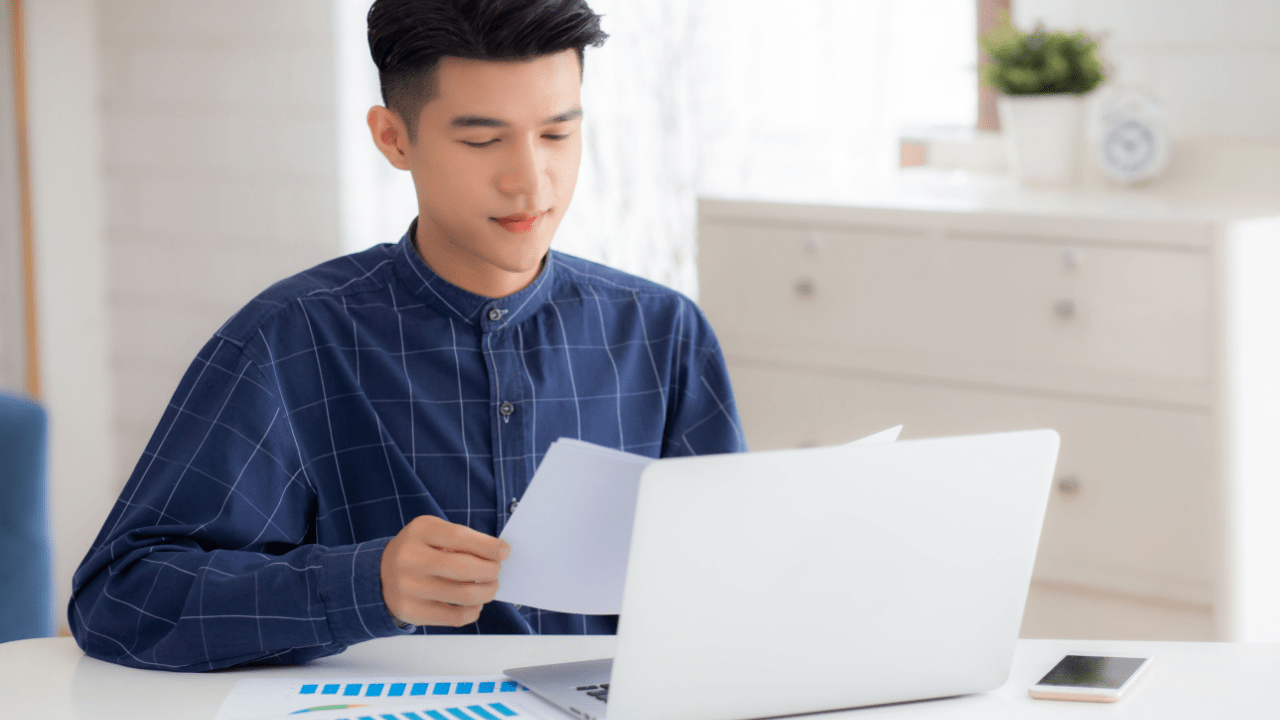 Young man reviewing financial documents on a laptop while considering if he should file bankruptcy for $20,000 in debt.