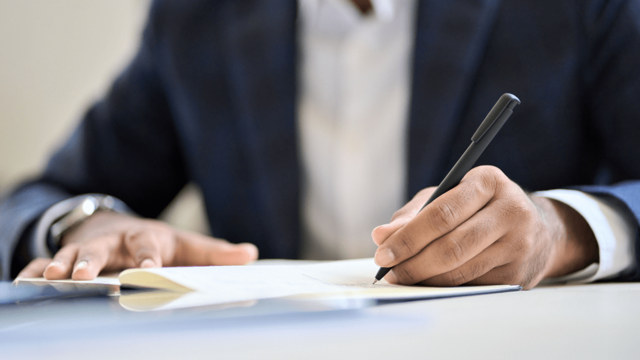 Close-up of a person in business attire signing financial paperwork, questioning if they should file bankruptcy for $10,000 in debt.