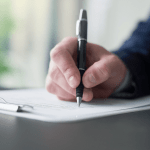 Close-up of a person signing official paperwork on a clipboard, representing the decision-making process around what is the minimum amount of debt for bankruptcy.