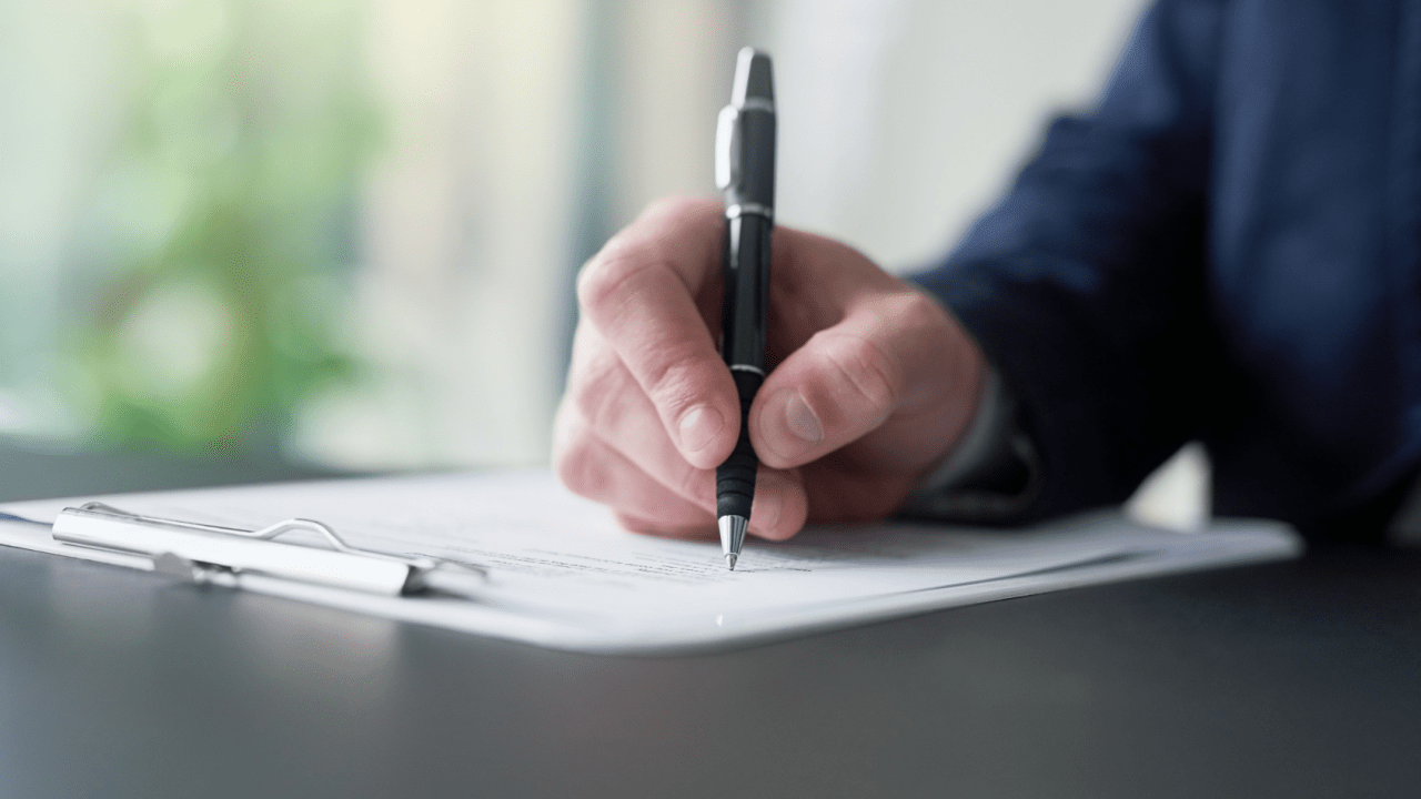 Close-up of a person signing official paperwork on a clipboard, representing the decision-making process around what is the minimum amount of debt for bankruptcy.