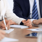 Business professionals discussing is paying someone to do SEO worth it while reviewing proposals and taking notes at meeting